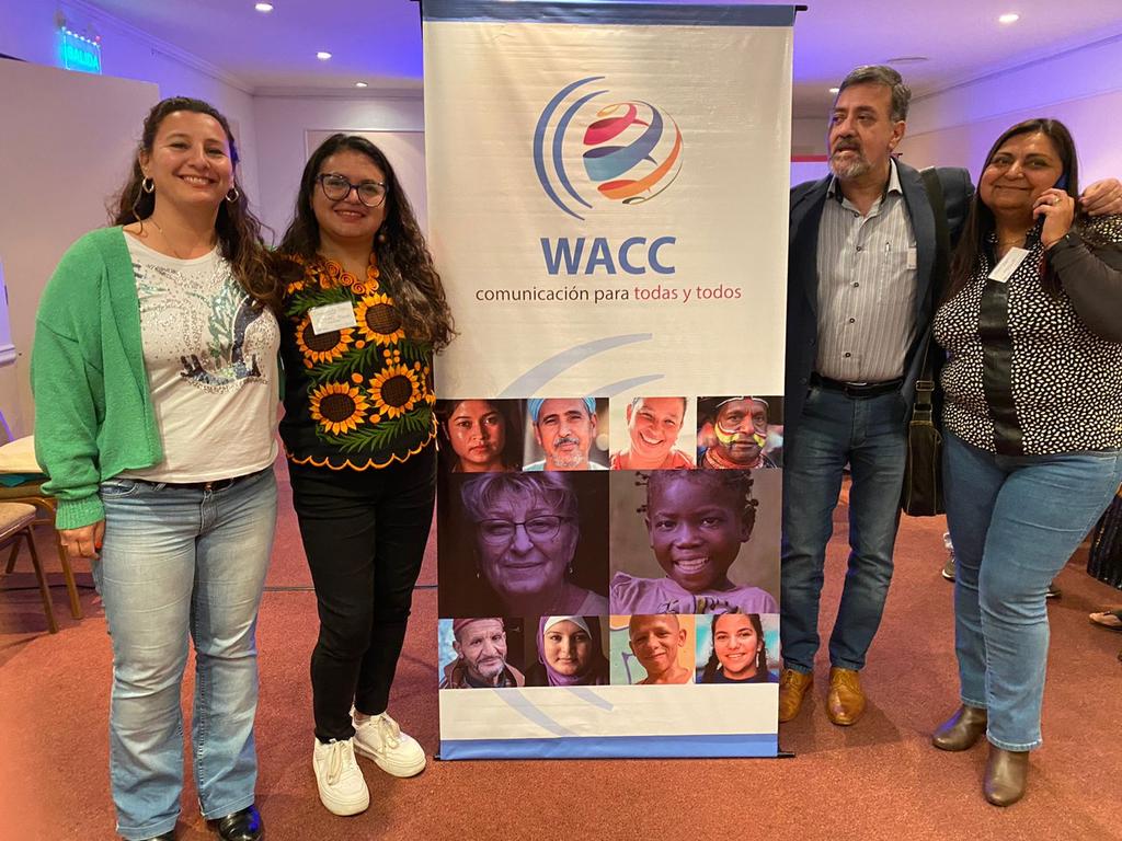 Three women and a man stand around a WACC banner