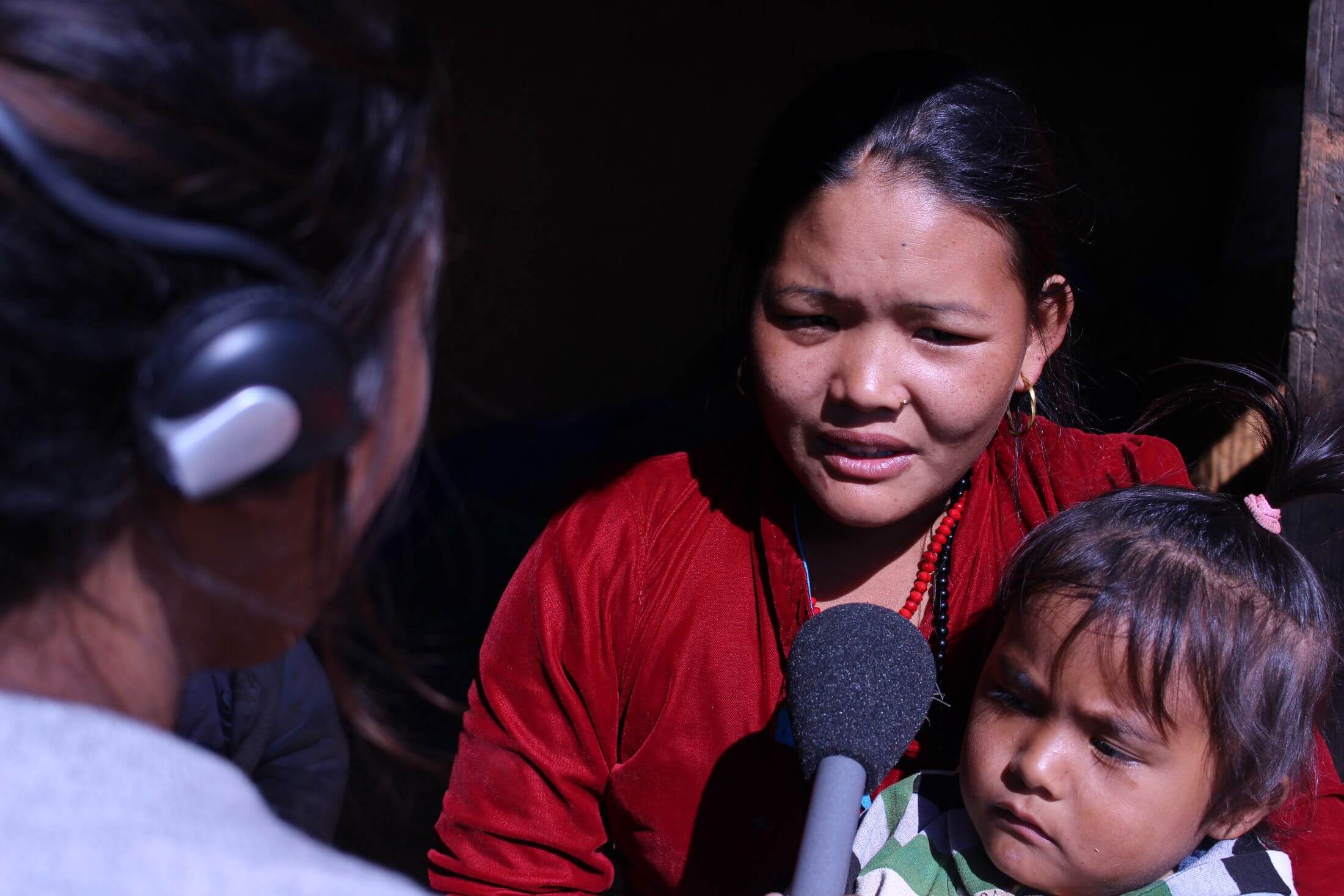Nepali woman holds a young child speaking into a microphone