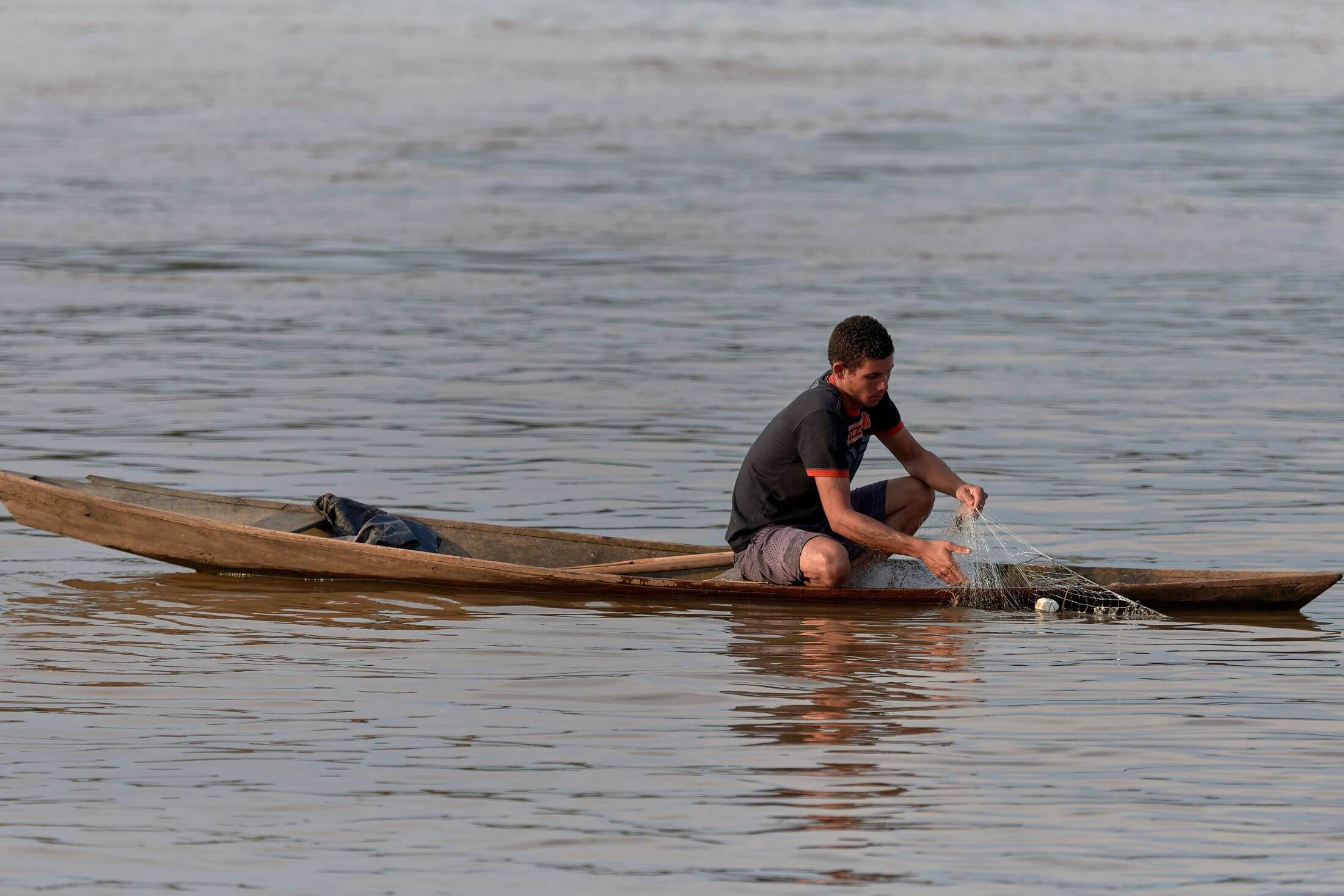 Man in a low-riding dugout canoe pulls in a fishing net